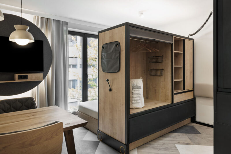 Raumteiler als offener Schrank mit Ablagen und Holzdetails trennt Wohn- und Schlafbereich.