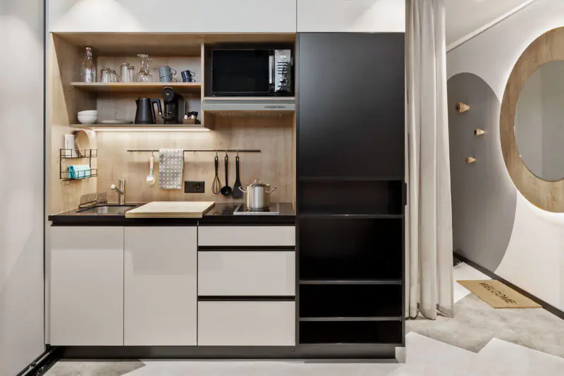 Kitchenette with sink, microwave, stovetop, coffee machine and mirror with hooks for clothes.