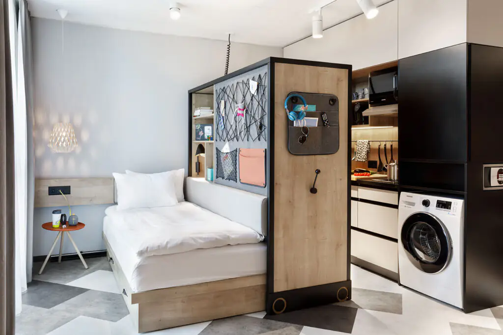Bright studio with bed, mesh element, armchair and kitchen in the background – modern interior design.